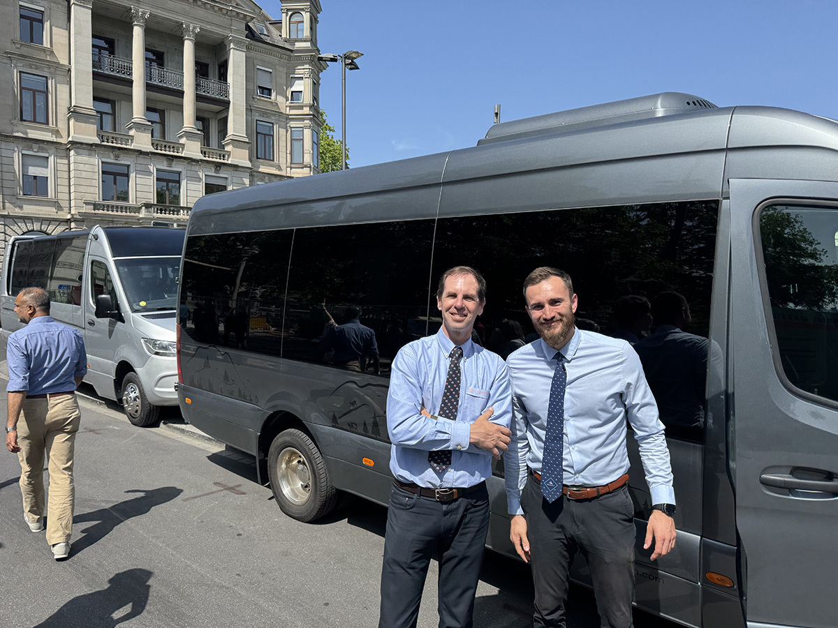 Employee welcoming guests beside a company vehicle